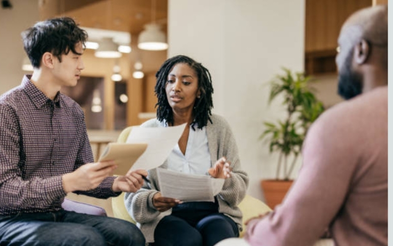 Two advisors reviewing documents with a student in a bright modern lounge
