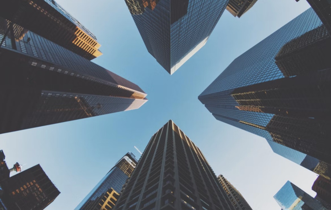 Glass skyscrapers seen from street level converging toward a clear blue sky